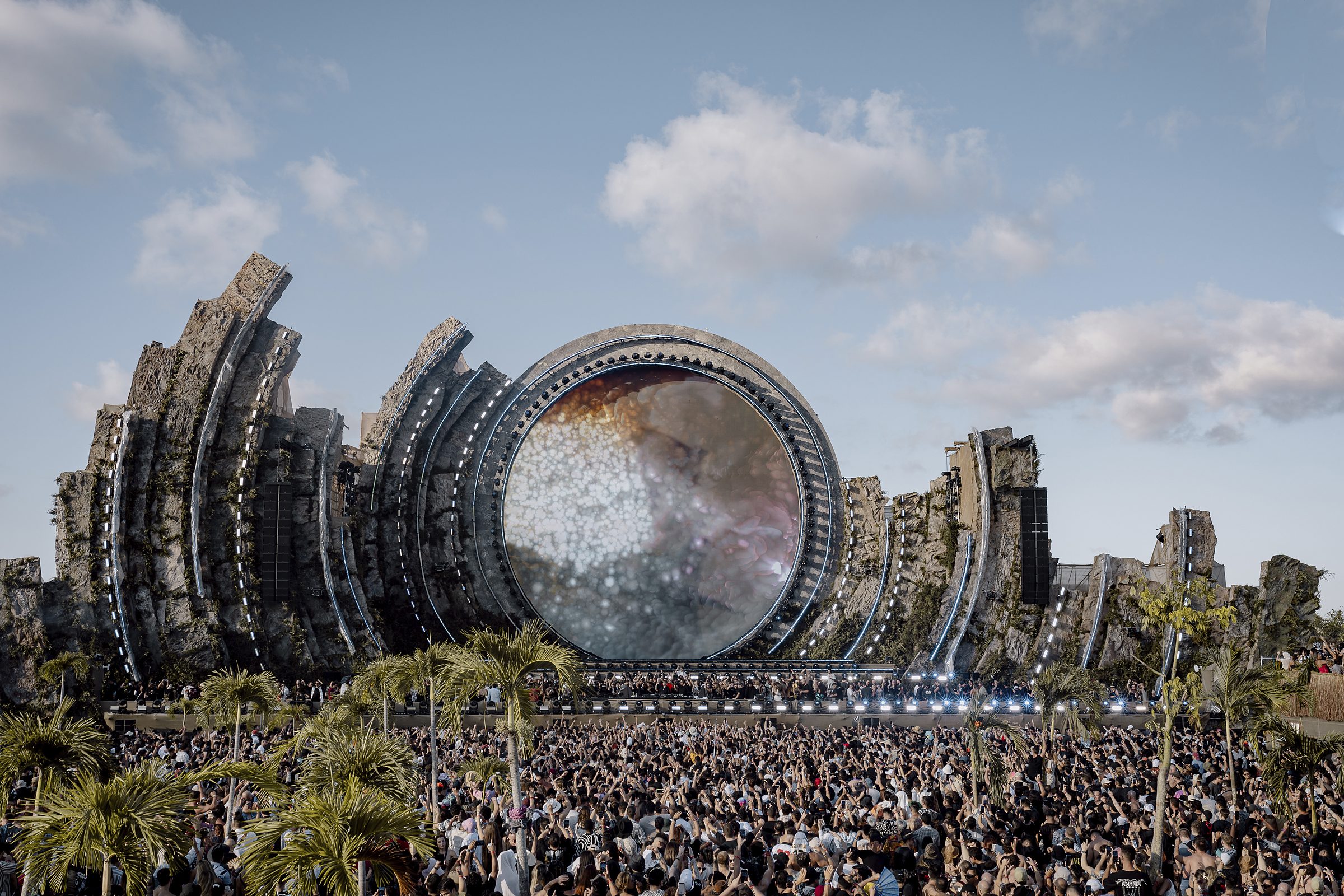 Crowd in front of a circular stage framed by rock structures and palm trees