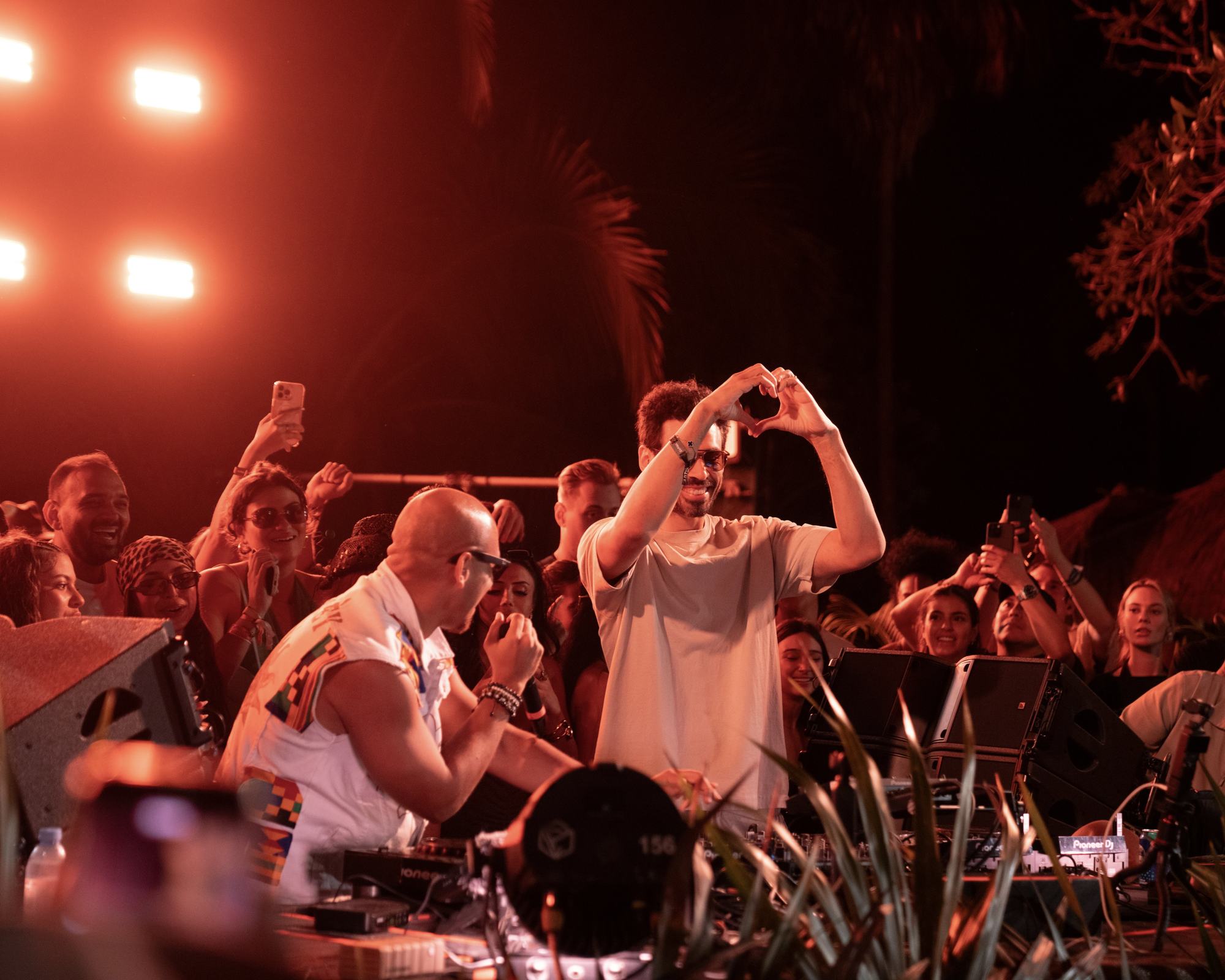 A DJ and the crowd making heart shapes with their hands at a Zamna party