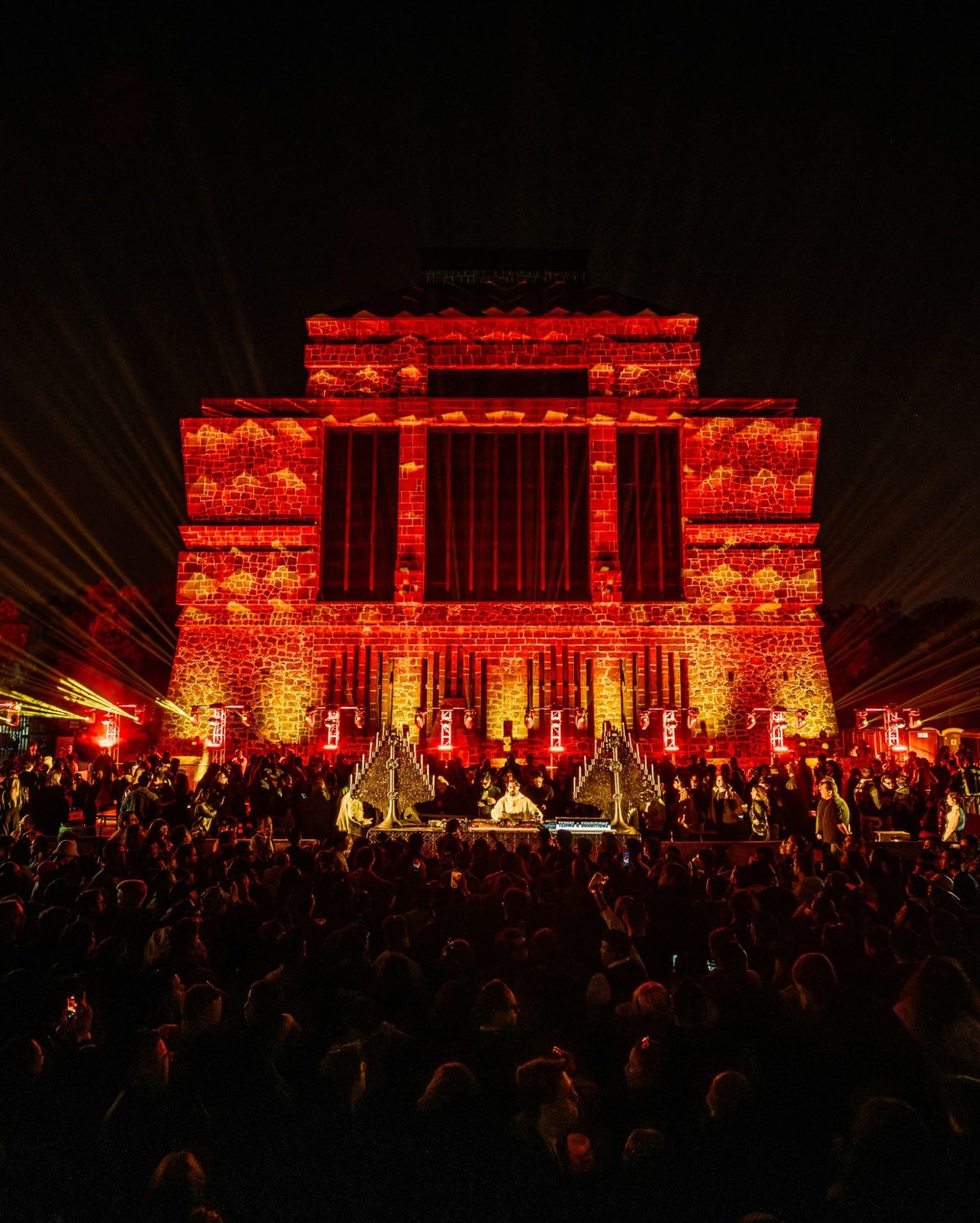Terms & Conditions DJ set in front of a stone building lit in red, with the crowd at night